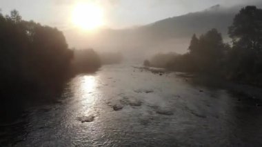 4K hava görüntüsü. Güneşli yaz sabahında köyü olan taze, hızlı dağ nehri üzerinde alçak irtifa uçuşu. Yeşil ağaçlar nehir ve güneş ışınları.
