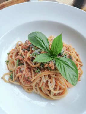 Beyaz tabakta domuz eti ve fesleğenli spagetti sosu..