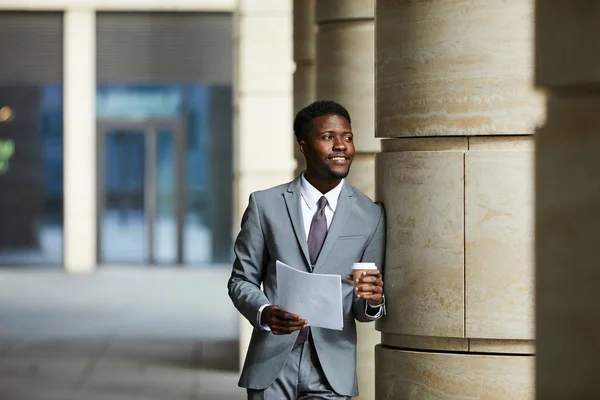 若いアフリカのビジネスマンは オフィスビルの読書文書や屋外でコーヒーを飲むの列にもたれてスーツを着て — ストック写真