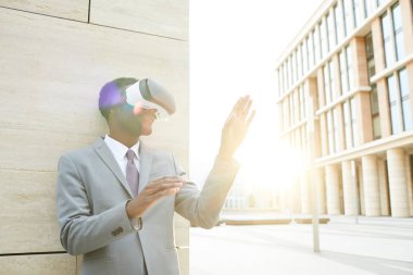 Sanal gerçeklik gözlüklü Afrikalı genç ofis müdürü dışarıda duruyor ve sanal toplantı yapıyor.