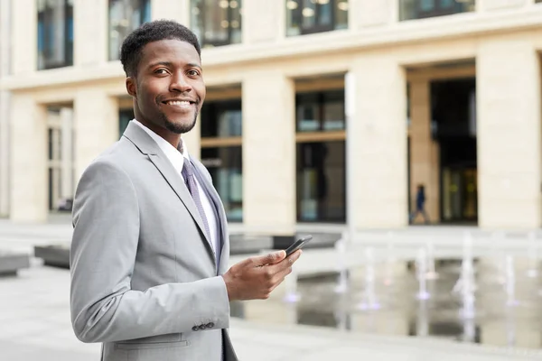 市内に立ち笑顔で携帯電話を持って訴訟におけるアフリカの若いビジネスマンの肖像画 — ストック写真
