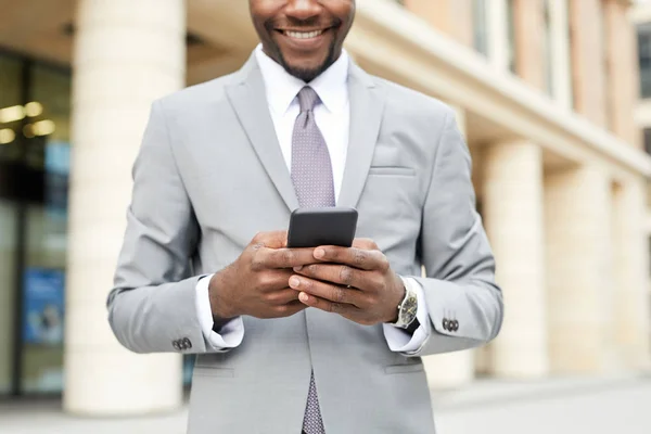 携帯電話でメッセージを入力し 笑顔市内に立って正式な服でアフリカの若いビジネスマンのクローズアップ — ストック写真