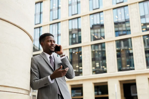 アフリカの自信に満ちたビジネスマンは 携帯電話で会話をしながら街に立つ — ストック写真
