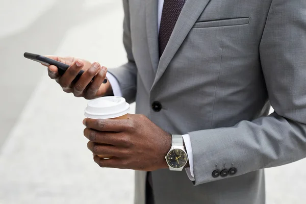 スーツに身を包んだアフリカ人ビジネスマンがコーヒーを飲みながら携帯電話を使って仕事をしている — ストック写真