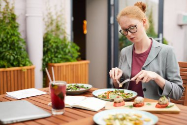 Açık kafede iş yemeği sırasında masada oturan ve sebze salatası yiyen genç bir kadının yakın çekimi.