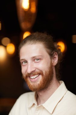 Beyaz tişörtlü, kameraya gülümseyen kızıl saçlı genç adamın portresi.