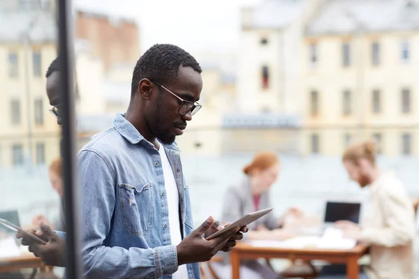 カフェの近くに屋外に立っている間 オンラインでデジタルタブレットを使用して通信眼鏡で深刻な若いアフリカ人男性 — ストック写真
