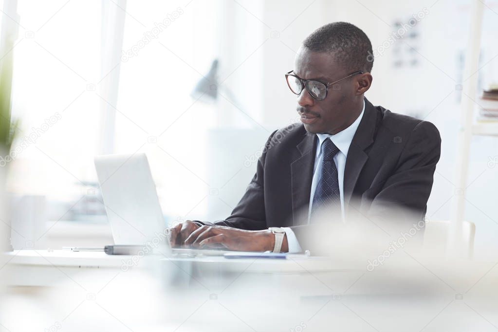 African male leader concentrating at work at office sitting at table and typing on computer