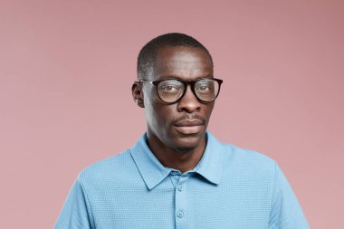 Gözlüklü ve sıradan giyinmiş, pembe arka planda kameraya bakan Afrikalı yakışıklı adamın portresi.