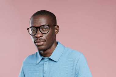 Gözlüklü ve sıradan giyinmiş, pembe arka planda kameraya bakan Afrikalı yakışıklı adamın portresi.