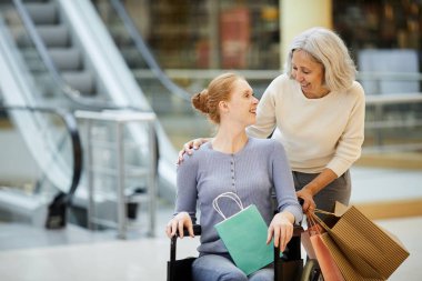 Mutlu kıdemli annenin portresi tekerlekli sandalyedeki engelli kızıyla birlikte, alışveriş torbaları ve gülümsüyor.