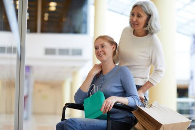 Tekerlekli sandalyedeki engelli kadın alışveriş merkezinde yaşlı annesiyle alışveriş yapıyor.