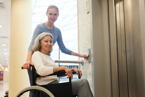 Genç bir kadın tekerlekli sandalyedeki engelli hastaya yardım ediyor.