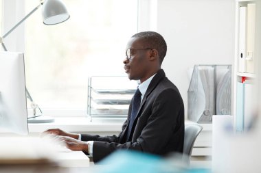 Ofiste işyerinde çalışırken bilgisayar monitörü ve yazma bakarak gözlüklü Afrikalı işadamıyan görünümü