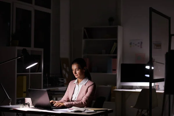 Genç Ciddi Bir Kadın Karanlık Bir Ofiste Lambanın Altında Oturup — Stok fotoğraf