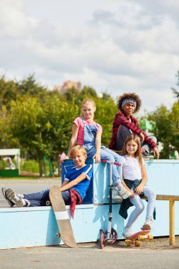 Parktaki kaykaylara bindikten sonra bankta oturup dinlenirken kameraya gülümseyen çocukların portresi.