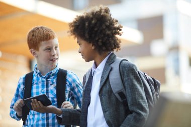 Two boys with bacpacks using mobile phone together after school 
