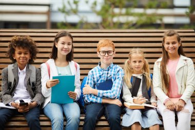 Bir grup okul çocuğu birlikte bankta oturup yeni materyalleri tartışıyor ve öğreniyorlar ve birlikte derse hazırlanıyorlar.