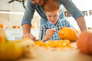 Küçük oğlum, Cadılar Bayramı partisi için babasıyla birlikte masada oturmuş balkabaklarını süslüyor.