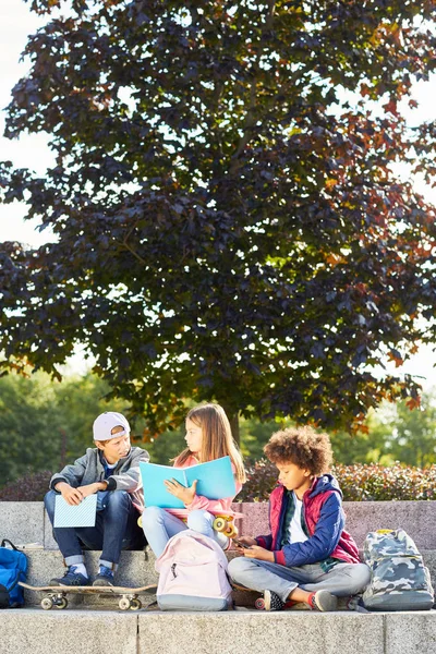 Group of friends sitting on stairs with books and skateboards and talking outdoors