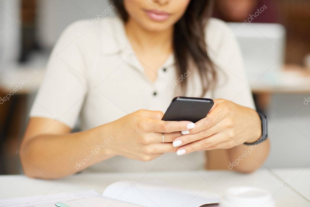 Close-up of young woman sitting at the table holding mobile phone and communicating online