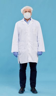 Koruyucu iş elbisesinde mavi arka planda dikilirken kameraya bakan olgun kimyagerin portresi