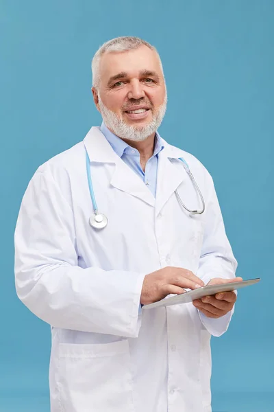 白髪と白のコートを持つシニア医師の肖像画は 青の背景にタブレットPc上でオンラインで動作 — ストック写真