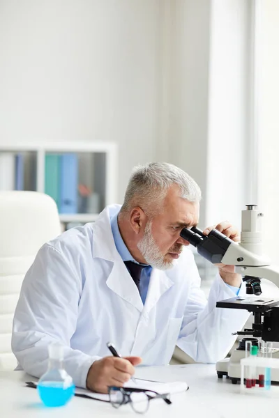 Grave Scienziato Maturo Concentrandosi Sul Lavoro Seduto Tavola Guardando Attraverso — Foto Stock