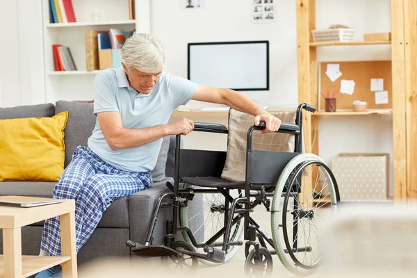 Старший Инвалид Сидит Диване Пытается Встать Опираясь Инвалидное Кресло Комнате — стоковое фото