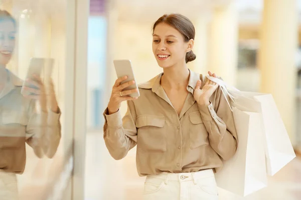 Jovem Mulher Elegante Ler Mensagem Telefone Celular Enquanto Segurando Sacos — Fotografia de Stock
