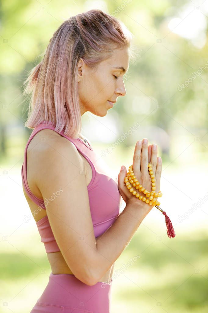 Side view of young healthy woman with amulet in hands standing with eyes closed and meditating during yoga outdoors