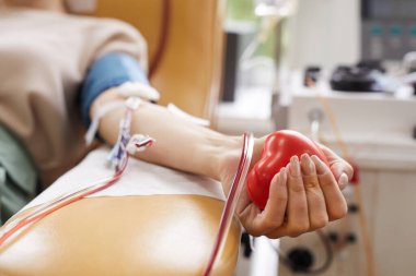 Close-up of patient with tubes in arm squeezing the ball in hand while donating the blood clipart