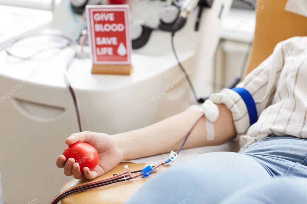 Close-up of female donor with ball in hand and in catheter in arm donating blood at hospital