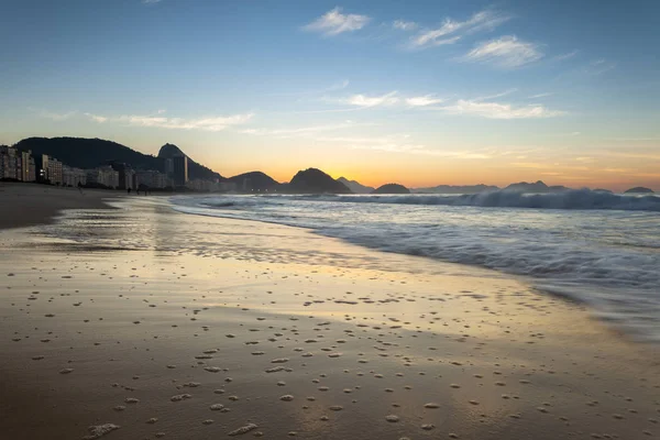 Early morning sunrise on Copacabana beach in Rio de Janeiro with the Sugarloaf mountain in the background and the wet sand showing air bubbles left by the waves