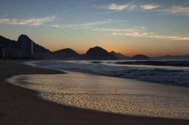 Desenler ve hava kabarcıkları gün doğumunda arka planda bir siluet olarak Sugarloaf dağ ile Rio de Janeiro Copacabana plajda gelen okyanus dalgaları tarafından sol