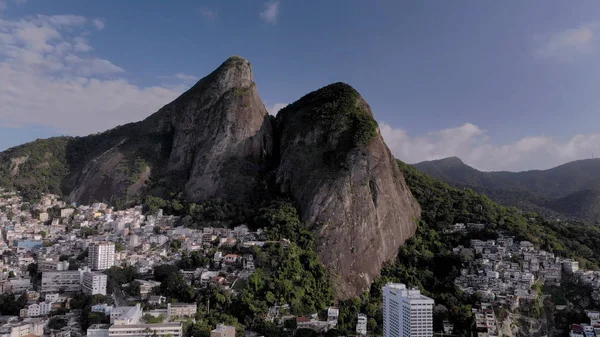 Aerial of Two Brothers mountain tops in Rio de Janeiro with the shantytown of Vidigal on its steep ascent. Skyline landscape of nature and dense urban shantytown community on the slopes.