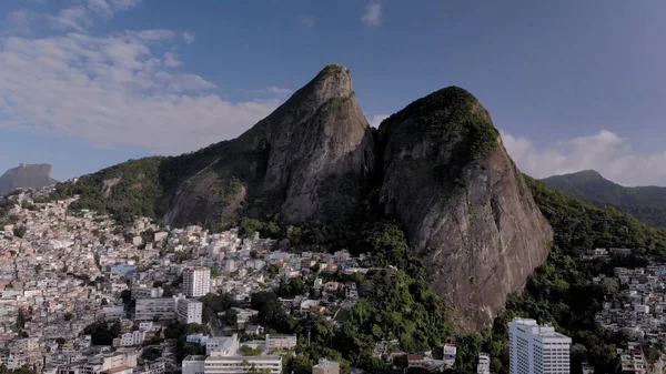 Aerial of Two Brothers mountain tops in Rio de Janeiro with the shantytown of Vidigal on its steep ascent. Skyline landscape of nature and dense urban shantytown community on the slopes.