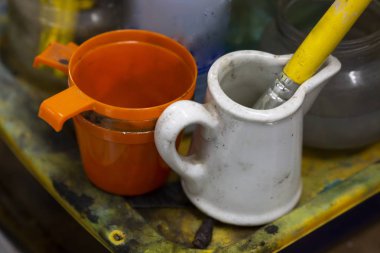 Bir sanatçı atölyesi yanı sıra turuncu plastik bir fincan ile beyaz bir küçük fincan batırılmış bir fırça natürmort yakın