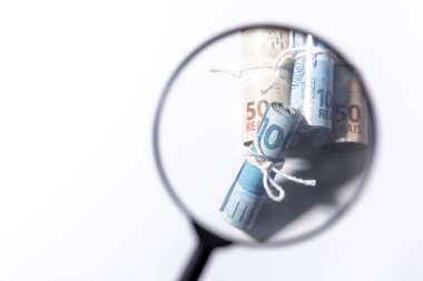 Odak dışında büyüteç banknot ruloları ayrı ayrı odak bir dize ile güvenli bakarak. Temiz stüdyo beyaz bir arka plan karşı büyütme aracı ile para vurdu.