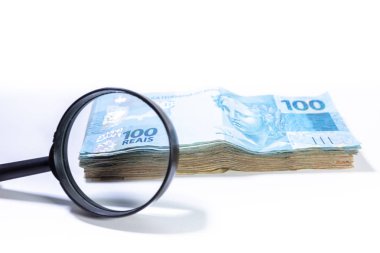 Yığının bir kısmına odaklanan büyüteçile Brezilya Reali banknot yığını. Temiz stüdyo beyaz bir arka plan karşı büyütme aracı ile para vurdu.