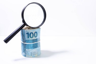 Arkadan aydınlatılmış bir büyüteç altında banknot kalın rulo. Temiz stüdyo beyaz bir arka plan karşı büyütme aracı ile para vurdu.