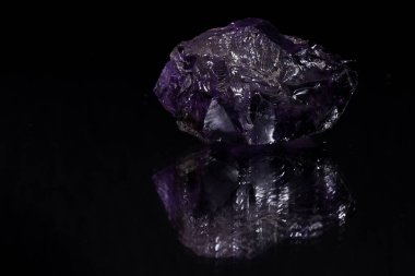 Rough cut big purple transparent stone with a black background reflecting in the surface it rests on clipart