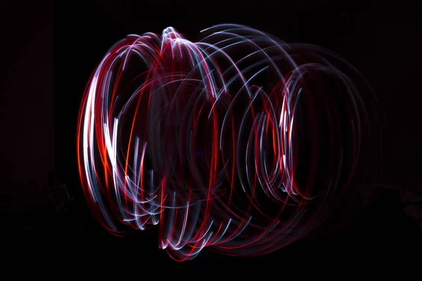 Light painting of continuous red and white spirals forming a chaotic vortex like figure. Dynamic time trajectory of two lights simultaneously against a black background.