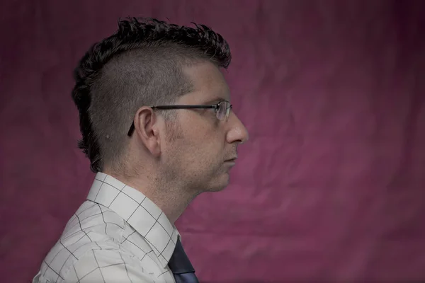 Profile face shot of a male punker with glasses, mohawk hairstyle, white striped shirt and  blue tie isolated on pink texturised background. Studio shot. Youth alternative culture.