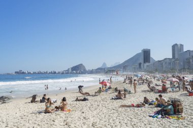 Rio de Janeiro, Brezilya-Ağustos 16, 2016: arka planda tipik mahalle manzarası ile mavi gökyüzü ile parlak güneşli bir günde Copacabana plaj ziyaretçileri