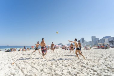 Rio de Janeiro, Brezilya-16 Ağustos 2016: arka planda tipik mahalle manzarası ile mavi gökyüzü ile parlak güneşli bir günde Copacabana plajında ayak voleybolu oynayan gençler grubu