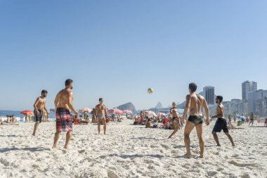 Rio de Janeiro, Brezilya-16 Ağustos 2016: arka planda tipik mahalle manzarası ile mavi gökyüzü ile parlak güneşli bir günde Copacabana plajında ayak voleybolu oynayan gençler grubu