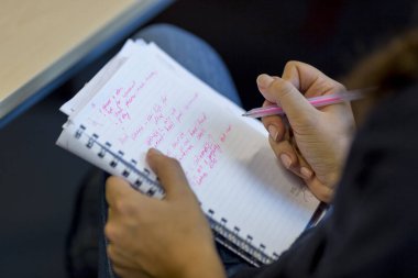 Sol el Mavi kot ile bir kadın bacak üzerinde bir defter tutarak sağ el ile pembe kalem ile yazmaya hazır notları yazarken