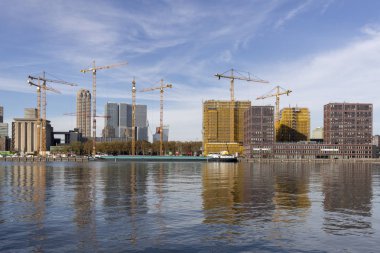 Hollanda 'nın Rotterdam kentinde mavi gökyüzü arka planı ile iskeledeki yüksek binalar üzerinde yükselen Vinçler