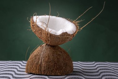 Koyu yeşil bir arka plan karşı bir desen yüzeyinde dış kahverengi kabuk ve iç beyaz coco ile bir kadeh oluşturan bir hindistan cevizi iki yarısı kapatın. Doğal bir kokteyl fincan Stüdyo kavramı.
